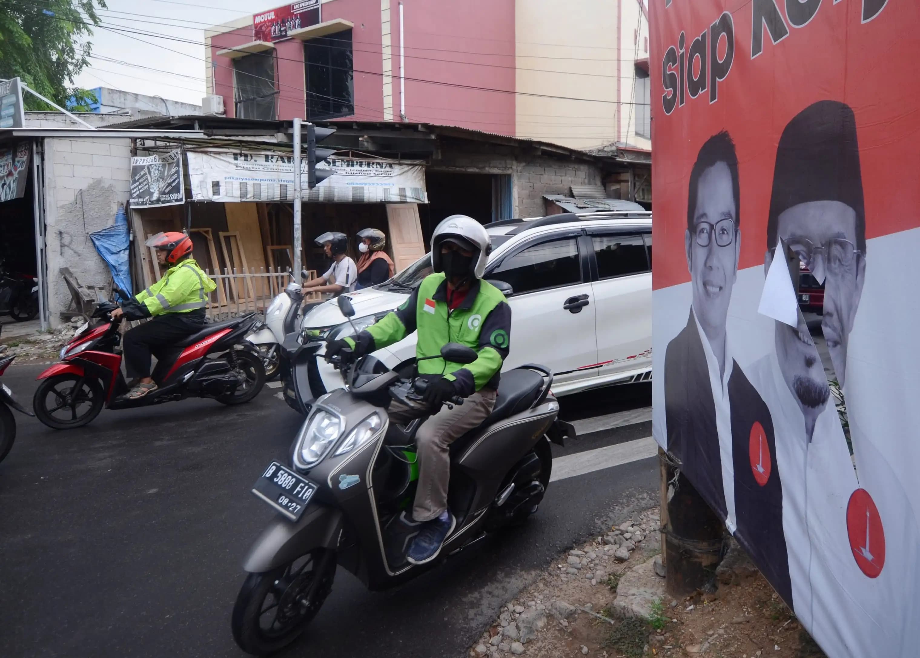 Warga melintasi baliho pasangan cagub-cawagub yang rusak (Foto: Dok MI/Donavita)