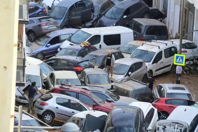 Seorang pria berdiri di atas kap mobil di antara kendaraan lain yang saling menumpuk (Foto: Getty Images)