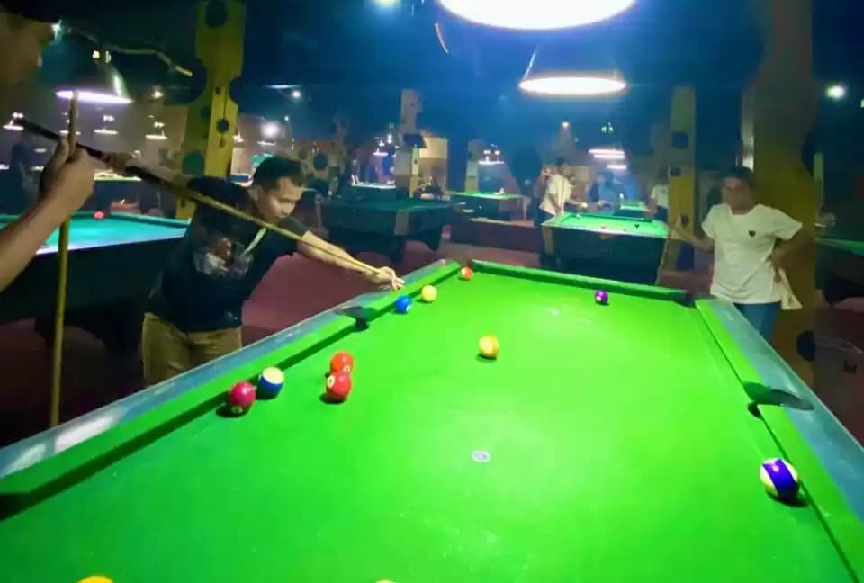 Seorang pemain Biliar sedang membidik bola memasukan kedalam lubang