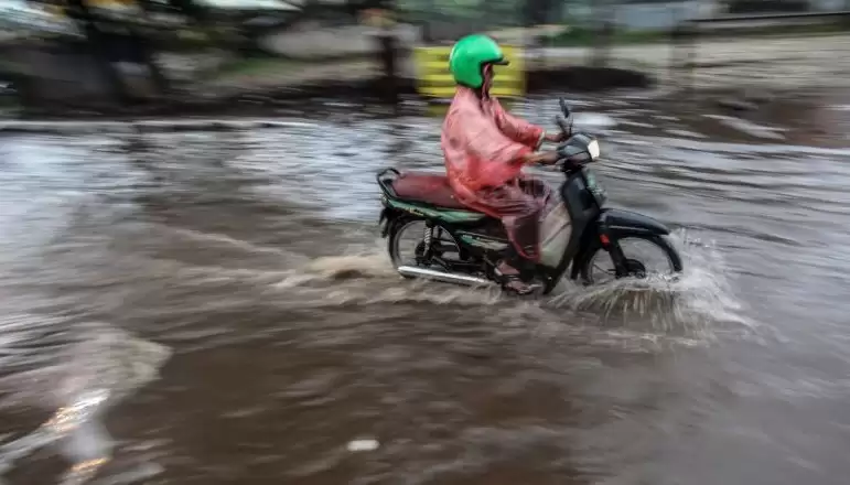 Pengendara sepeda motor melintasi genangan air. [Foto: Antara]