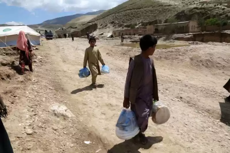 Dua orang anak berjalan membawa bantuan banjir di Distrik Borka, Provinsi Baghlan, Afghanistan, pada 12 Mei 2024. (Foto: Xinhua)