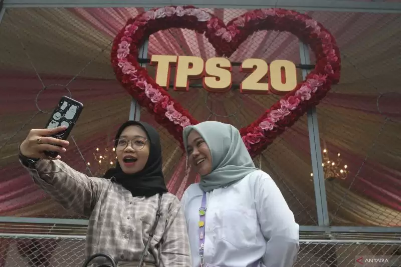 Pemilih melakukan swafoto di depan dekorasi bertema hari kasih sayang, di TPS 20 di Kelurahan Gadingkasri, Kota Malang, Jawa Timur, Rabu (14/2). [Foto: ANTARA/Ari Bowo Sucipto]