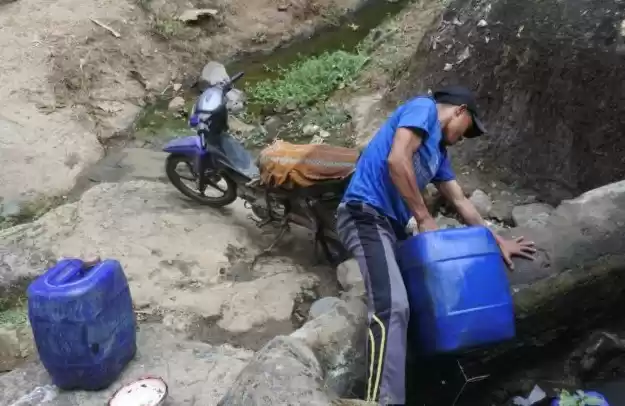 Seorang warga mengambil air di sumber mata air yang mengecil di Desa Curahtatal, Arjasa, Situbondo. (Foto: Antara)