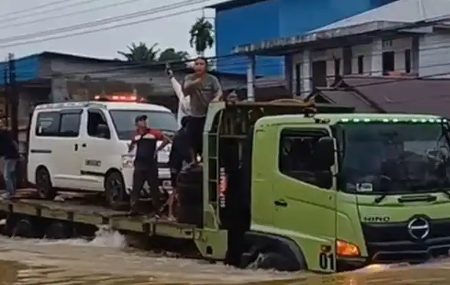Mobil ambulans terpaksa dinaikan keatas mobil pengangkut alat berat menyebrangi banjir. (Foto: Antara)