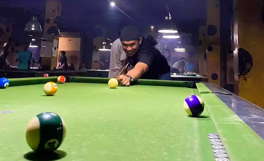 Seorang pemain Biliar sedang membidik bola memasukan kedalam lubang